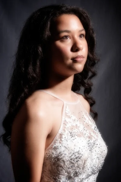 A dramatic studio portrait with sculpted light and elegant styling. Dramatic studio portrait of a woman in a white dress looking upward.
