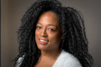 A warm studio portrait with soft light and natural expression. Studio portrait of a woman with curly hair against a gray background.