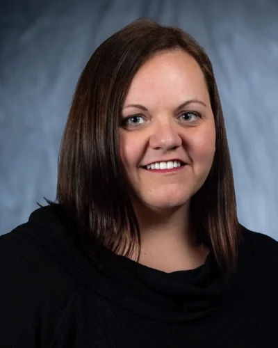 A polished professional headshot with friendly expression and studio lighting. Professional headshot of a smiling woman against a blue studio background.