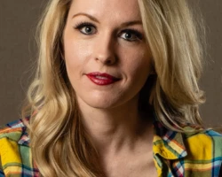 A confident editorial portrait with bold styling and direct eye contact. Editorial portrait of a blonde woman wearing a colorful plaid shirt.