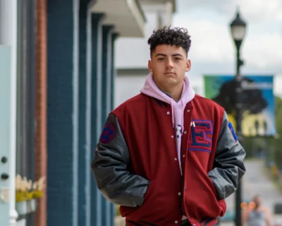 Senior portrait with downtown character. Outdoor senior portrait of a young man wearing a red letter jacket and pink hoodie on a downtown sidewalk.