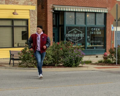 Downtown environmental senior portrait. Environmental senior portrait of a young man in a red letter jacket walking in front of a downtown coffeehouse.