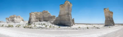 Monument Rocks rise from the Kansas plains in stark sunlight. White chalk rock formations standing in an open Kansas landscape beneath a blue sky.