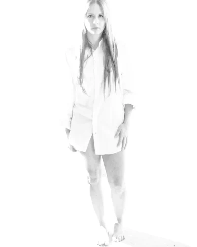 Soft, high-key portrait study in white. High-key black and white portrait of a woman standing in an oversized white shirt against a nearly white background.