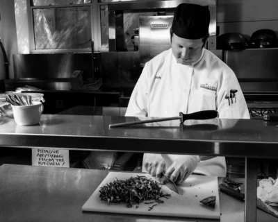 A chef works carefully at the prep station in a professional kitchen. Black and white photo of a chef preparing food in a professional kitchen.