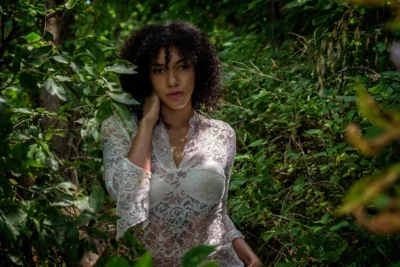 A natural environmental portrait framed by lush green foliage. Environmental portrait of a woman in a white dress surrounded by greenery.