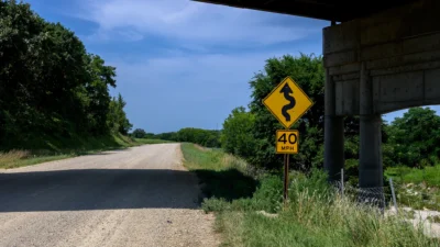 Deep Creek Road, Kansas Color photograph of a gravel section of Deep Creek Road in Kansas passing under a bridge beside a winding road sign.