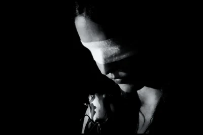 Blindfolded portrait with rose. Dramatic black and white portrait of a blindfolded woman holding a rose in low directional light.