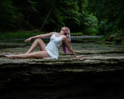 Reclining figure in a wooded creek bed. Fine-art environmental portrait of a woman reclining on a rock ledge above a shallow creek in a wooded setting.