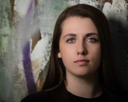 A clean senior portrait with a calm expression and textured urban-style background. Senior portrait of a young woman against a textured painted wall.
