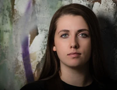 A clean senior portrait with a calm expression and textured urban-style background. Senior portrait of a young woman against a textured painted wall.