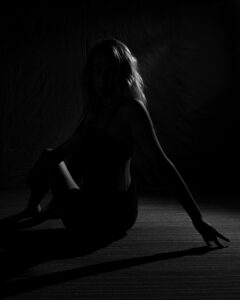 Low-key black-and-white portrait of a seated woman outlined by rim light